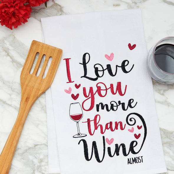 flour sack kitchen towel with an embroidered phrase of I love you more than wine surrounded by little hearts on a marble counter