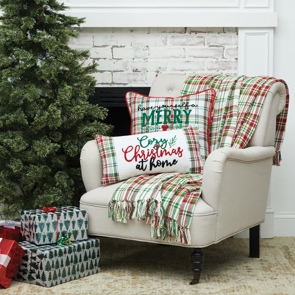 red green and white plaid woven throw with tassels and matching holiday pillows on a chair next to a tree and presents