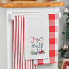 waffle weave towel with the phrase Joy to the World nestled between a wreath and above a snow covered town decorated for the holidays hanging from a kitchen counter