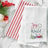 waffle weave towel with the phrase Joy to the World nestled between a wreath and above a snow covered town decorated for the holidays on a marble countertop