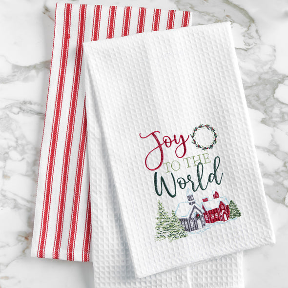 waffle weave towel with the phrase Joy to the World nestled between a wreath and above a snow covered town decorated for the holidays on a marble countertop