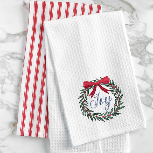 waffle weave towel with a wreath topped with a red bow and the word joy in the center on a marble countertop