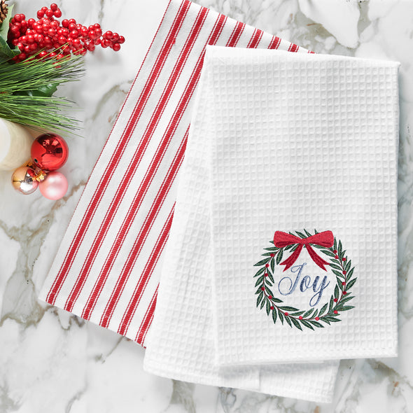 waffle weave towel with a wreath topped with a red bow and the word joy in the center on a marble countertop