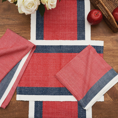 woven table linens with red centers and outlined in blue with white borders on a wood table with flowers and apples