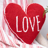 heart shaped red hooked pillow with the word love in white text on a chair with a red and white blanket