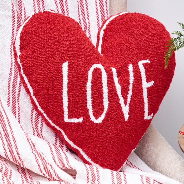 heart shaped red hooked pillow with the word love in white text on a chair with a red and white blanket