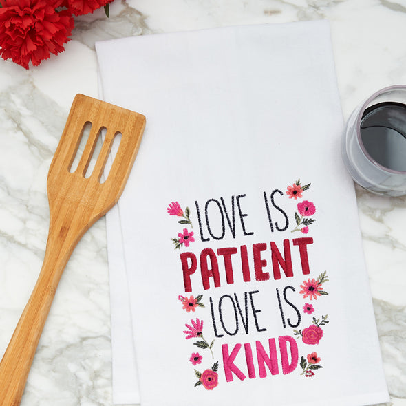 embroidered flour sack towel with the phrase love is patient love is kind surrounded by flowers on a marble kitchen counter