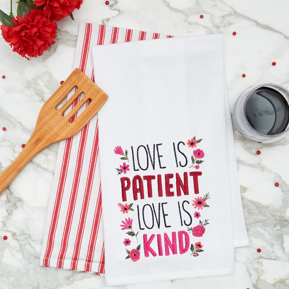 embroidered flour sack towel with the phrase love is patient love is kind surrounded by flowers on a marble kitchen counter