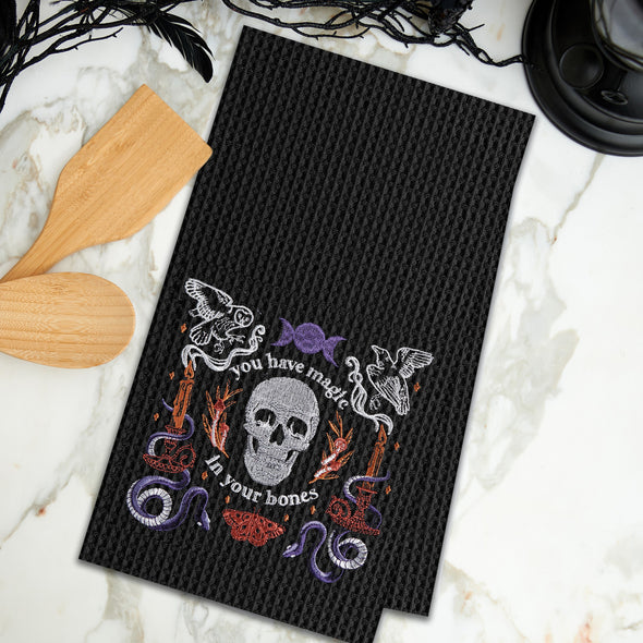 black waffle weave towel with a skull and the phrase you have magic in your bones surrounded by mystical elements on a marble countertop