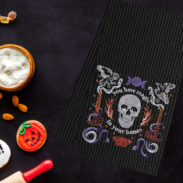 black waffle weave towel with a skull and the phrase you have magic in your bones surrounded by mystical elements next to Halloween candy