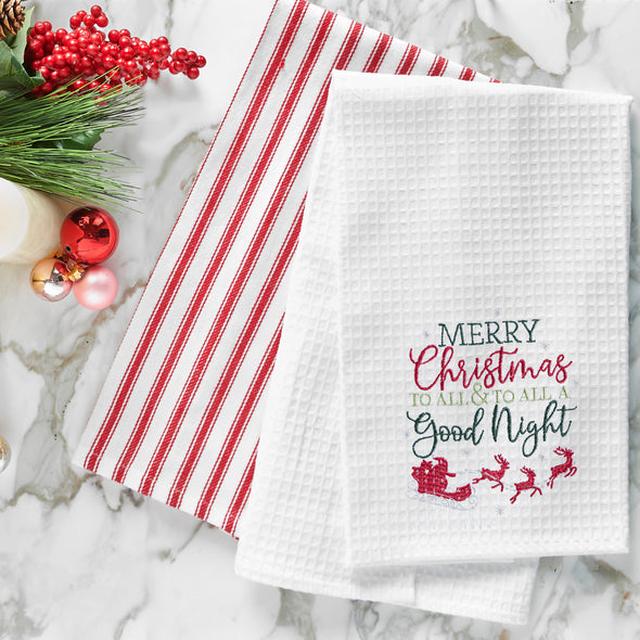 waffle weave towel with the phrase Merry Christmas to All & To All a Good Night in different fonts above Santa in his sleigh flying with his reindeer on a marble countertop