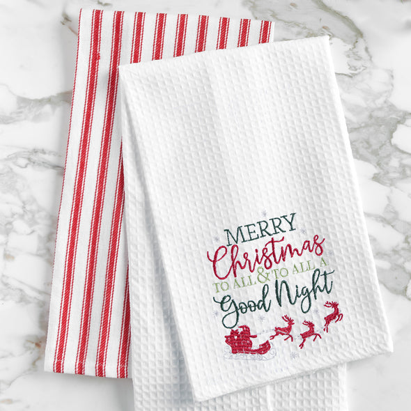 waffle weave towel with the phrase Merry Christmas to All & To All a Good Night in different fonts above Santa in his sleigh flying with his reindeer on a marble countertop