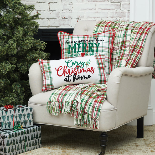 applique and tufted pillow with the phrase have yourself a merry little Christmas on a plaid pillow in red and green. a holly berry and leaves sits in the center of the pillow with tufted berries on a chair with matching decor next to a Christmas tree and presents