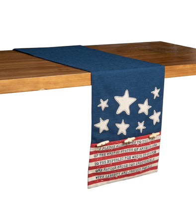 a printed and applique table runner that features a blue center panel and edges adorned with white stars and red and white stripes that have patriotic text on the white sections