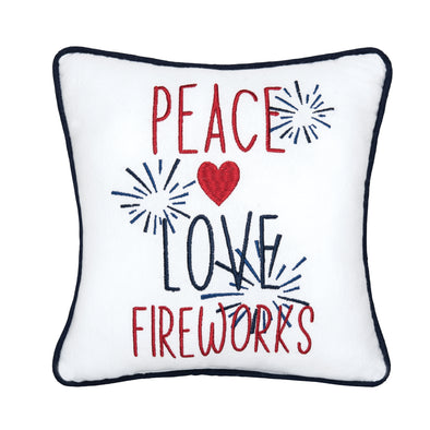 an embroidered pillow with modern font that reads peace love fireworks surrounded by bursting fireworks and a heart. the entire pillow is trimmed in a complementary navy blue.