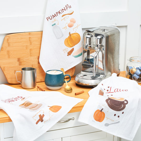 set of three illustrated food and recipe related kitchen towels set up in a kitchen setting