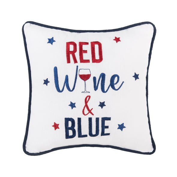 an embroidered white pillow trimmed in blue with the words red wine and blue in bold lettering surrounded by delicate blue and red stars. the "I" in wine is shaped like a wine glass filled with red wine