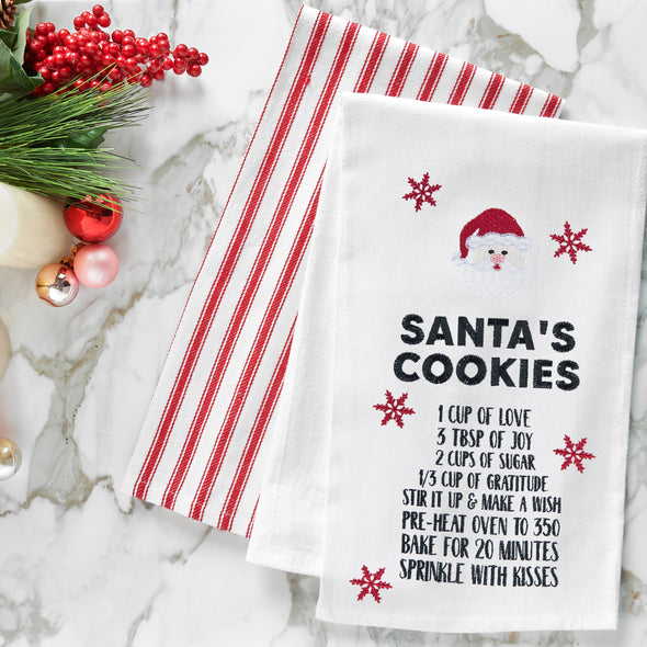 embroidered flour sack towel with instructions to make Santa's cookies including ingredients like love, joy, and sugar below a picture of Santa's face and surrounded by red snowflakes on a marble countertop