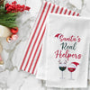 embroidered flour sack towel with the phrase Santa's real helpers above two glasses of holiday decorated wine on a marble countertop