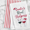 embroidered flour sack towel with the phrase Santa's real helpers above two glasses of holiday decorated wine on a marble countertop