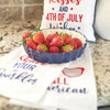 flour sack towel with the words shake your sparkler in flourishing text surrounded by sparklers in red and blue with sparks of yellow paired with additional patriotic decor and a dish of strawberries