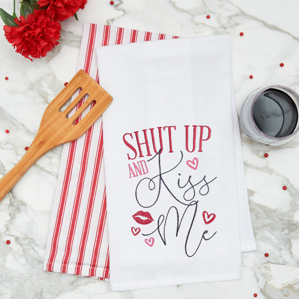 embroidered flour sack towel with the phrase shut up and kiss me surrounded by red lips and hearts on a marble kitchen counter