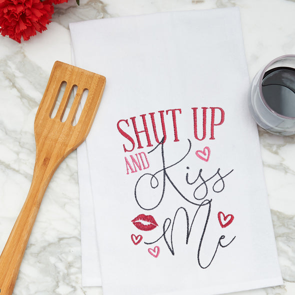 embroidered flour sack towel with the phrase shut up and kiss me surrounded by red lips and hearts on a marble kitchen counter