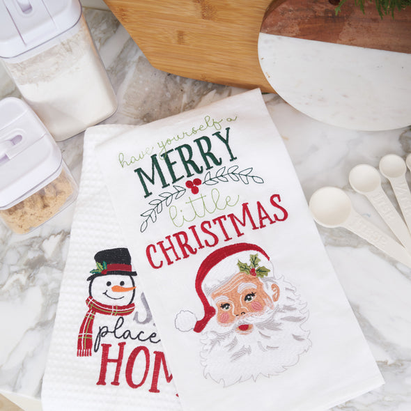 waffle weave towel with a snowman wearing a top hat and scarf next to the phrase there's snow place like home on a marble countertop paired with a towel reading have yourself a merry little Christmas with Santa's face