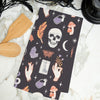 black printed kitchen towel with mystical motifs including skulls, potion bottles, snakes, bats, and crystal balls on a marble countertop