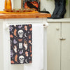 black printed kitchen towel with mystical motifs including skulls, potion bottles, snakes, bats, and crystal balls hanging from a kitchen counter