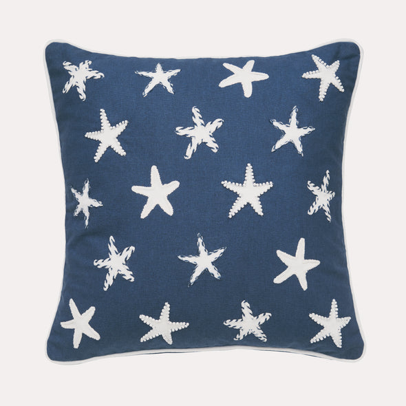 a printed and embellished pillow with a navy blue background and covered with a scattering of starfish making it but coastal and patriotic.