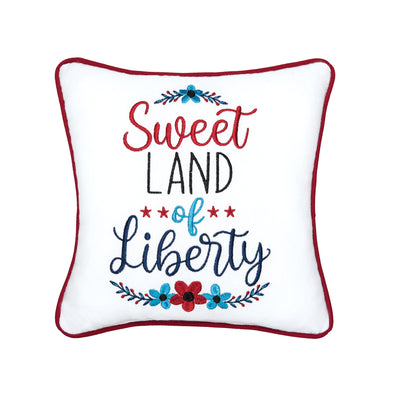 an embroidered pillow with the phrase sweet land of liberty in the center and a botanical and floral motif on the top and bottom while the entire pillow is trimmed in red