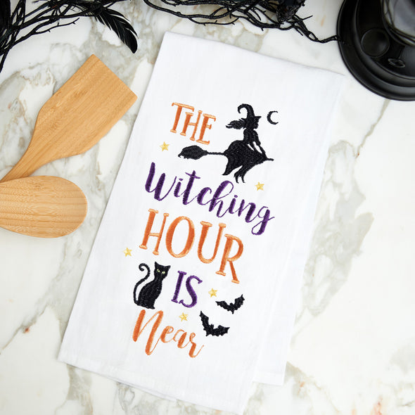 flour sack towel with embroidered Halloween icons including a witch, black cat, and bats on a marble counter