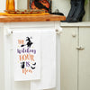 flour sack towel with embroidered Halloween icons including a witch, black cat, and bats hanging from a kitchen counter