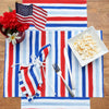 watercolor inspired printed table linens in patriotic red white and blue hues on a wood table with popcorn in a bowl and a mason jar of flowers and an American flag