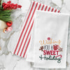 embroidered flour sack towel with the phrase wishing you a sweet holiday surrounded by classic Christmas sweets including a gingerbread man, peppermint candy, hot cocoa, and candy cane on a marble countertop