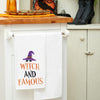 flour sack towel with embroidered phrase of witch and famous topped with a witches' hat and stars hanging from a kitchen counter