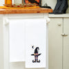 embroidered waffle weave towel with a black witches' hat and legs next to a halfmoon and stars hanging from a kitchen counter