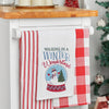 embroidered flour sack towel with the phrase Walking in a Winter Wonderland above a snow globe featuring a snowman in a winter scene next to a tree hanging from a kitchen countertop