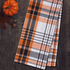 woven orange black and white plaid kitchen towel on a wood table next to a pumpkin