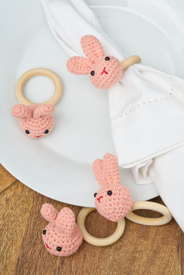 pink knitted napkin rings in use on a white napkin laid on a dinner plate