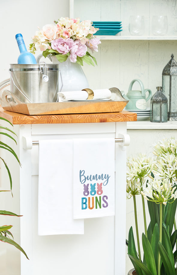 bunny buns embroidered in spring colors on white flour sack kitchen towel draped over a kitchen counter