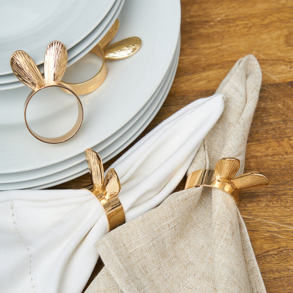 gold metal bunny ears napkin rings laid on a dining room table