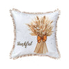 White pillow featuring an embroidered bundle of wheat with the word Thankful stitched in script