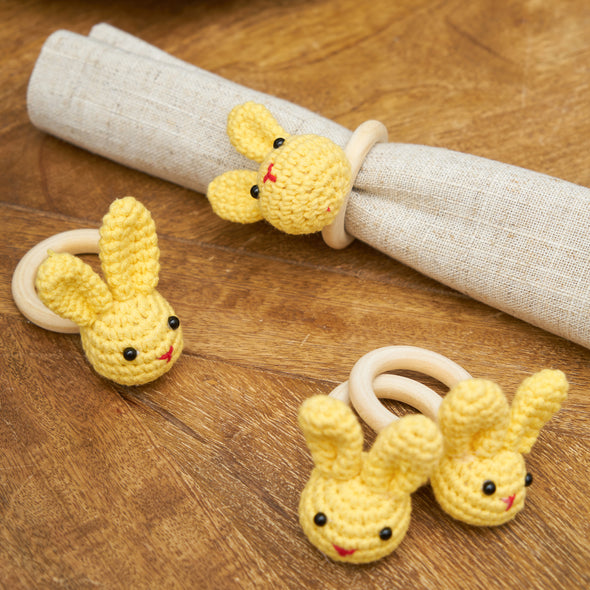 yellow knitted napkin rings in use on a tan napkin laid on a dining room table